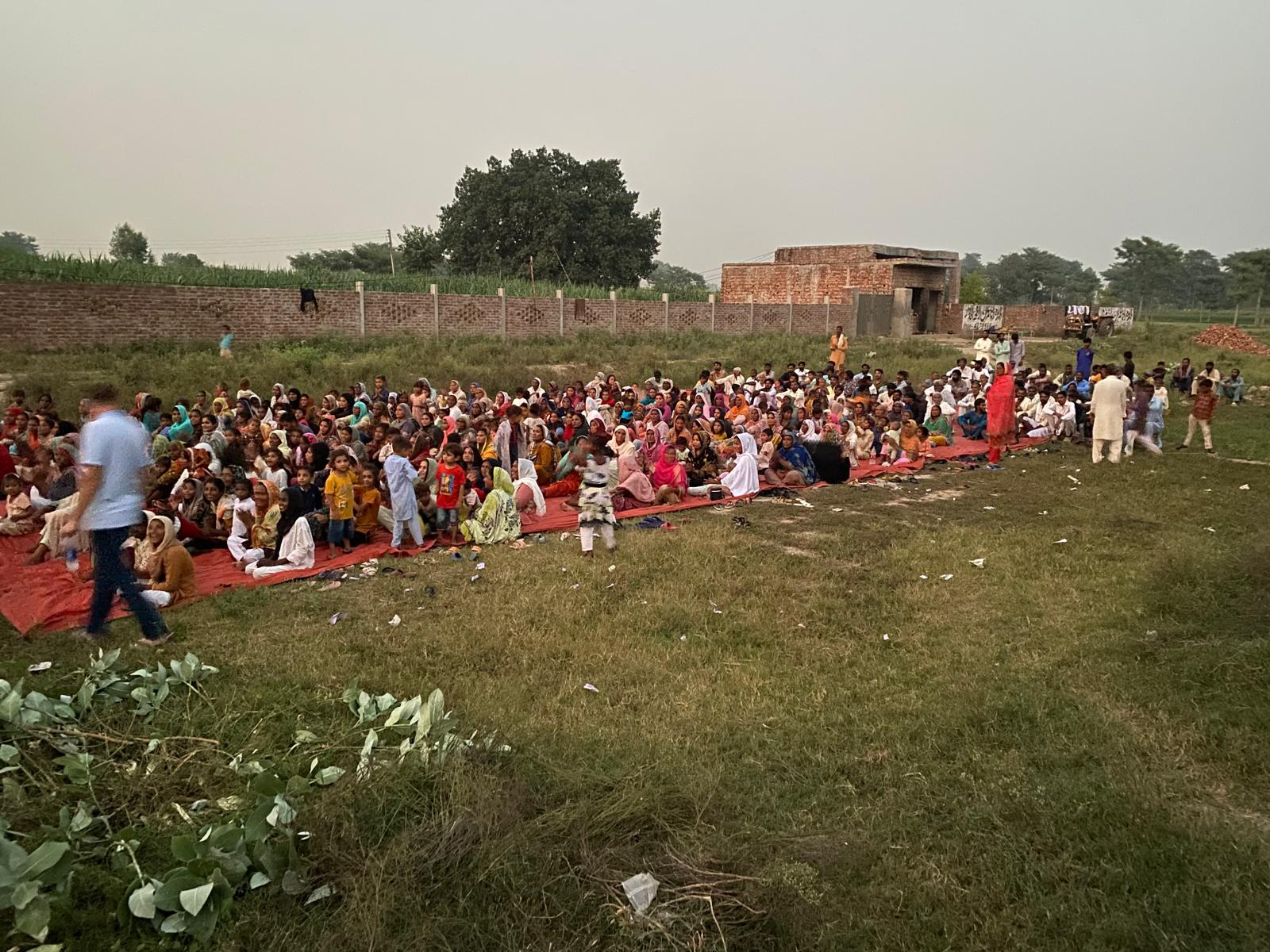 A large outdoor gathering seated on the grass in Pakistan