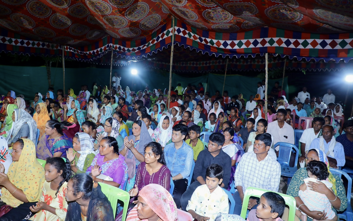 Large crowd gathered under a canopy for an evening meeting