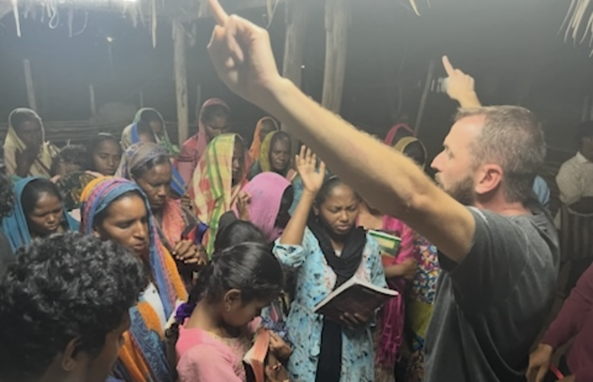 Leading a village gathering in prayer with hands raised