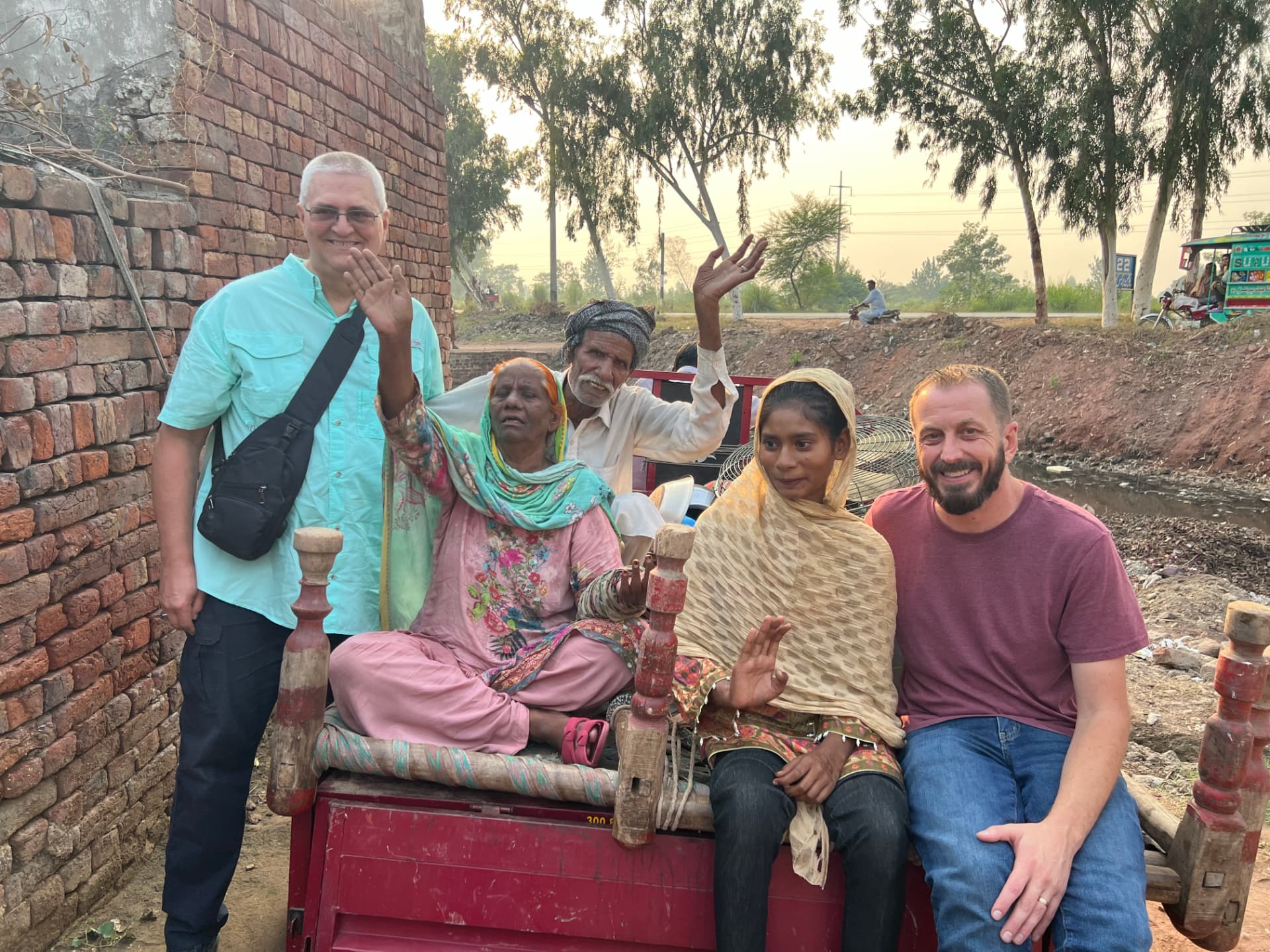 A joyful family and ministry partners waving together from a cart in Pakistan