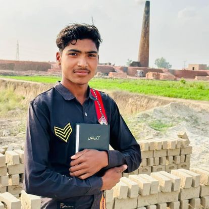 A young man holding a Bible in front of a brick kiln in Pakistan