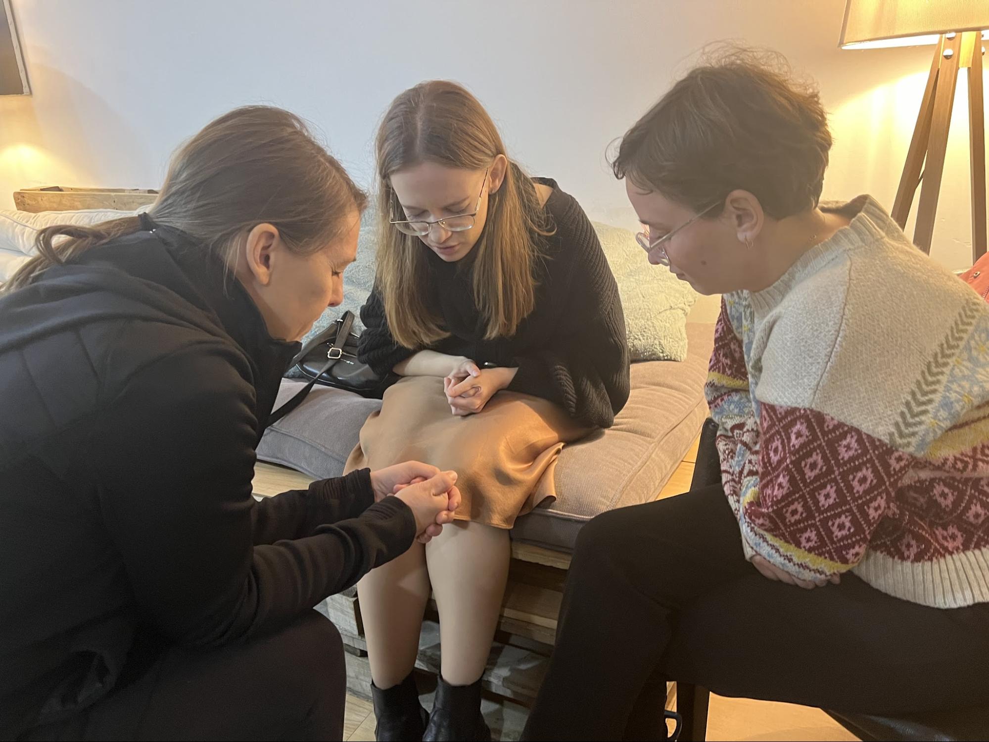 Three women praying together in a living room