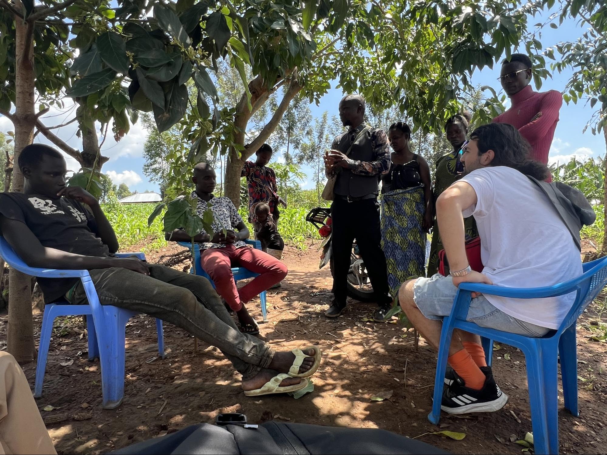 Outdoor gathering of believers seated under shade trees
