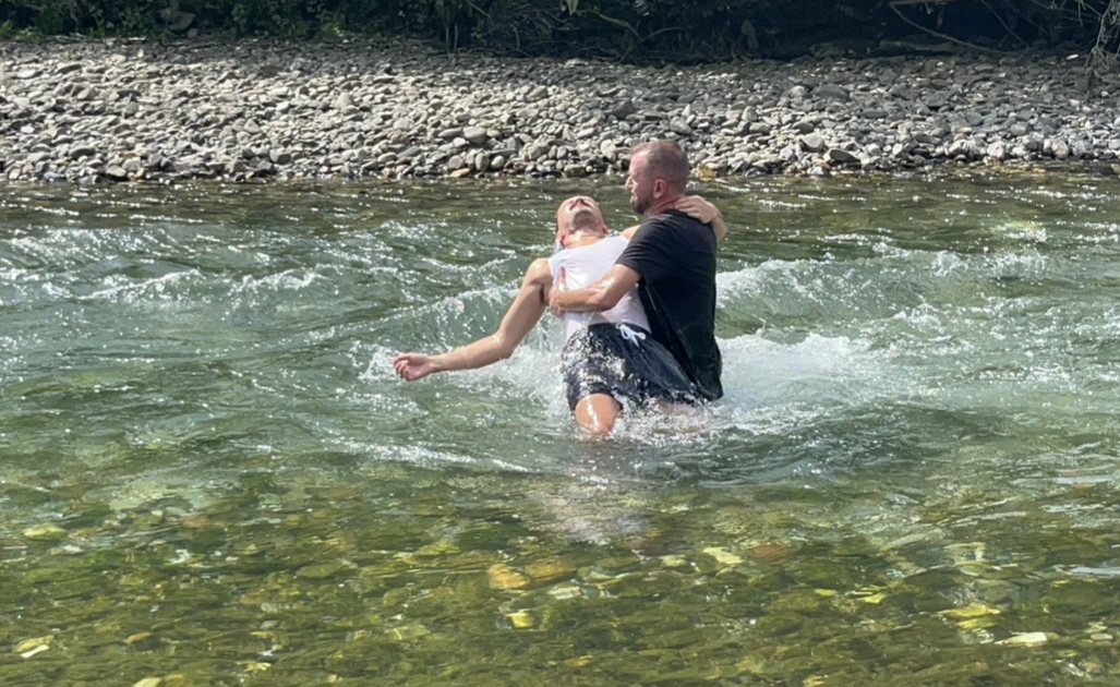 Two men being baptized in a clear mountain river
