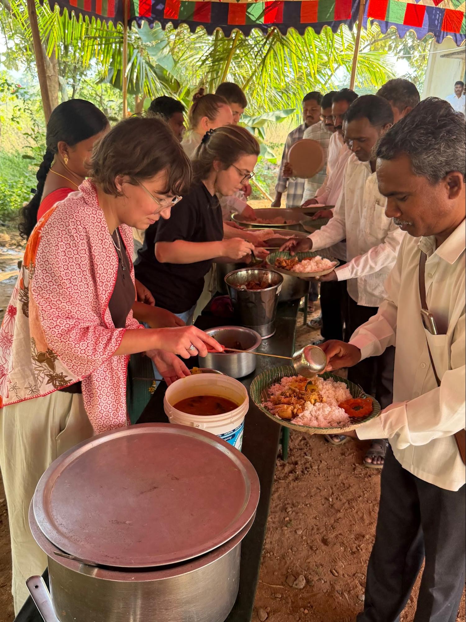 Team serving rice and curry to guests under a festive canopy