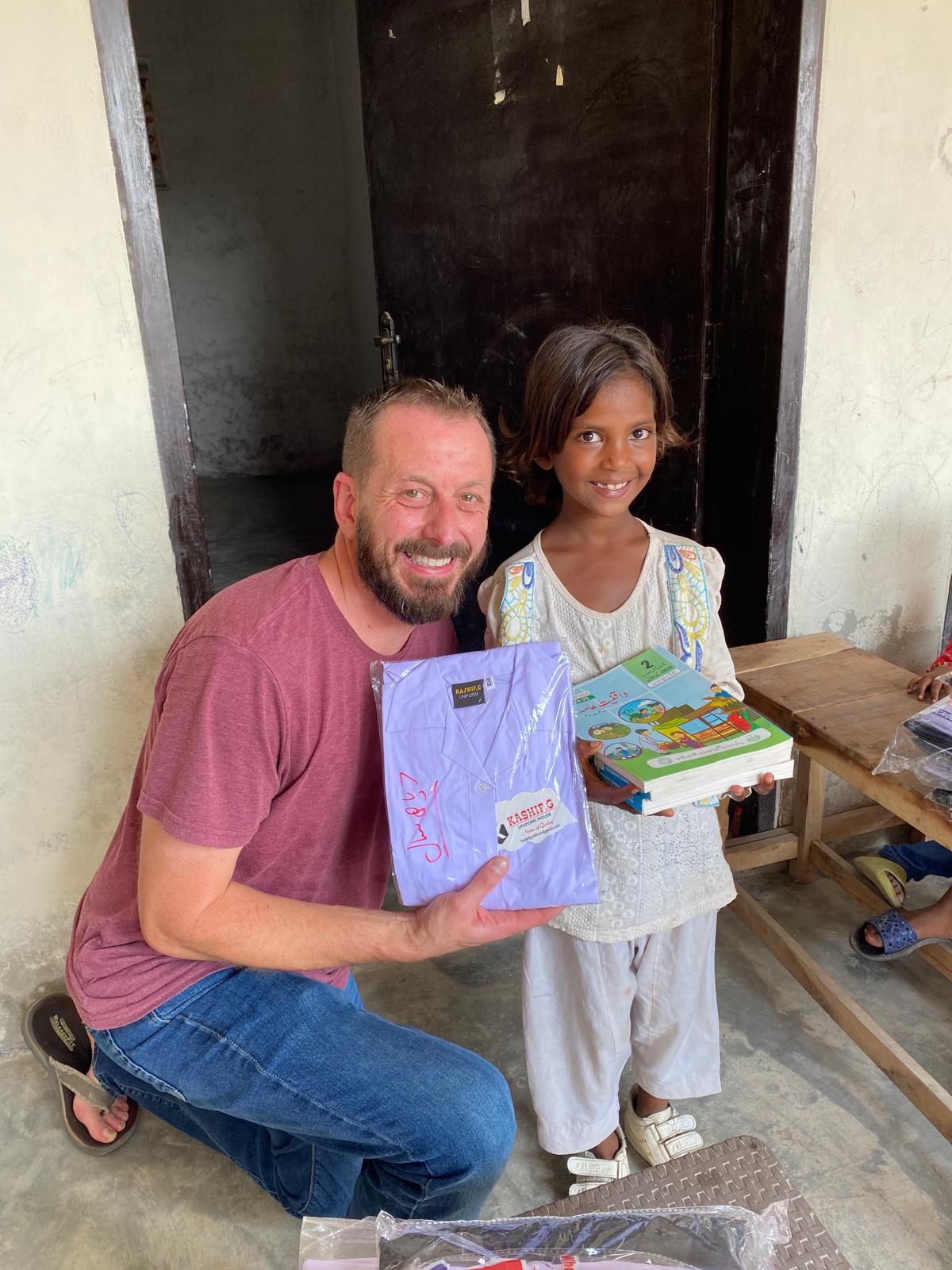 A ministry partner giving a school uniform and books to a child in Pakistan