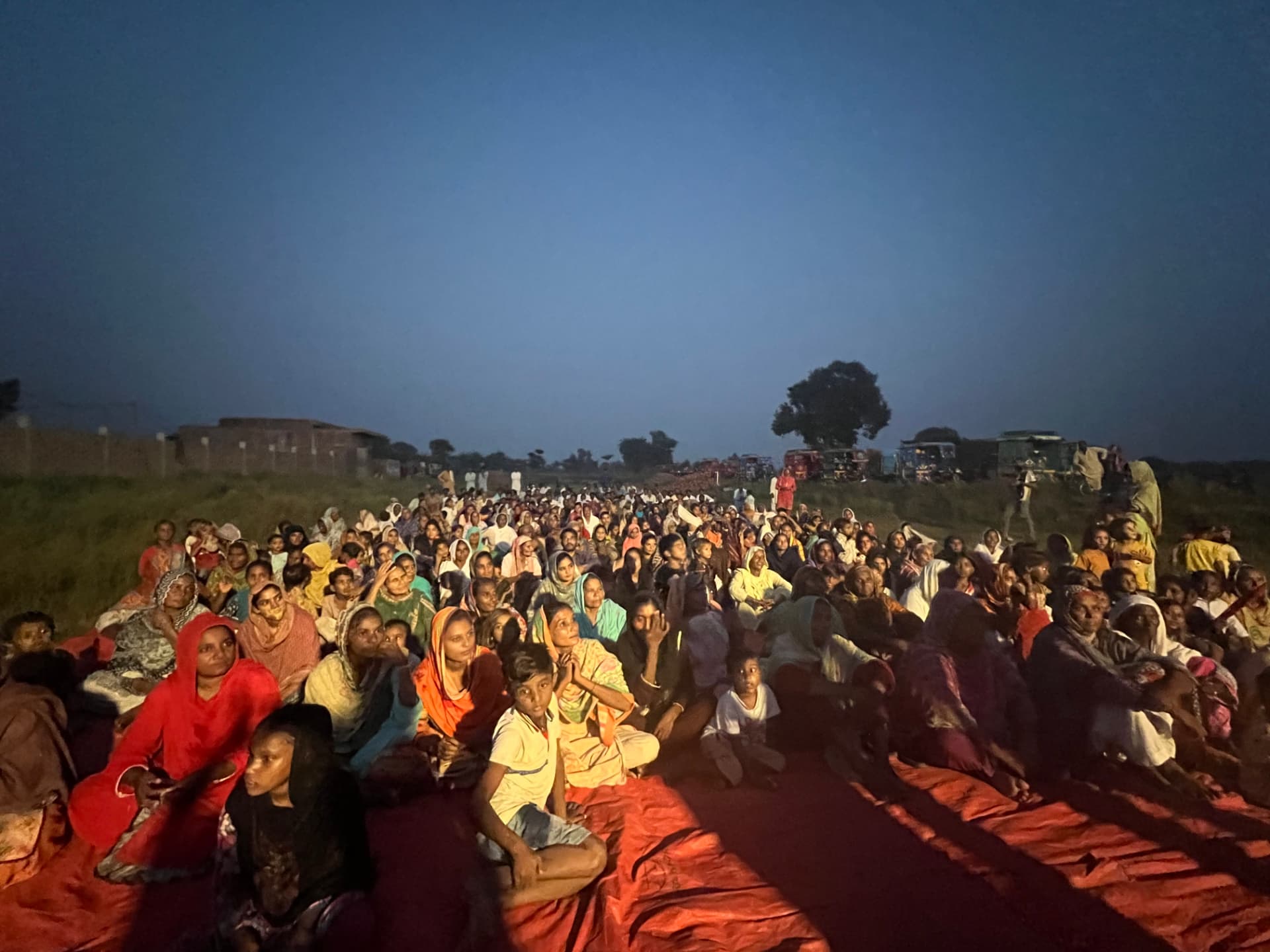 A large outdoor evening gathering seated on blankets in Pakistan