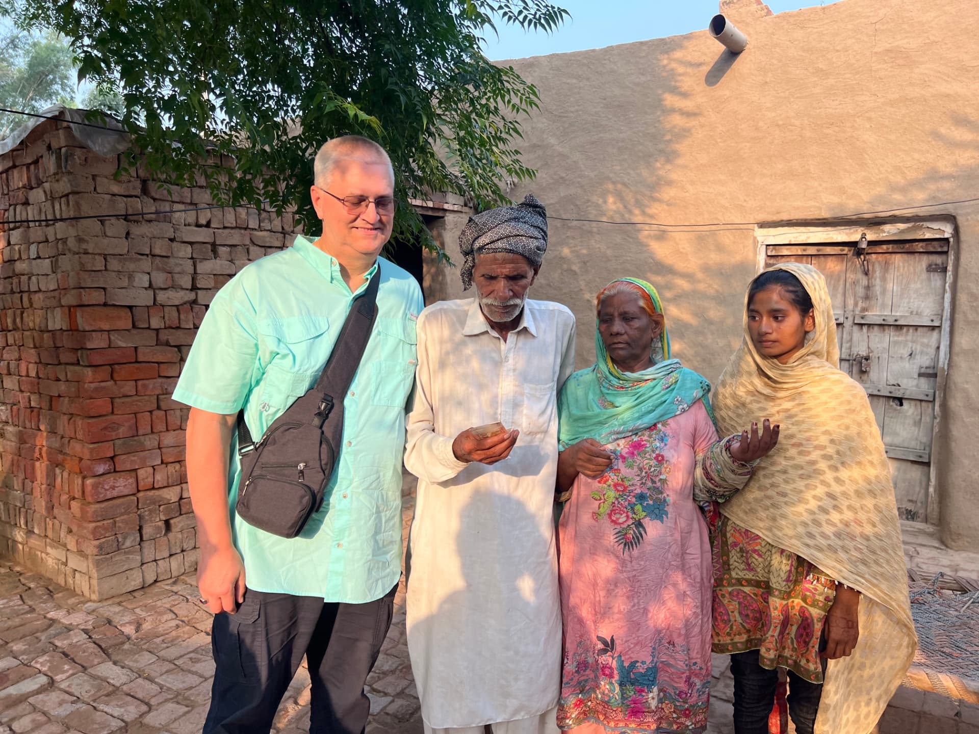 A ministry partner standing with a family outside their home in a rural Pakistani community