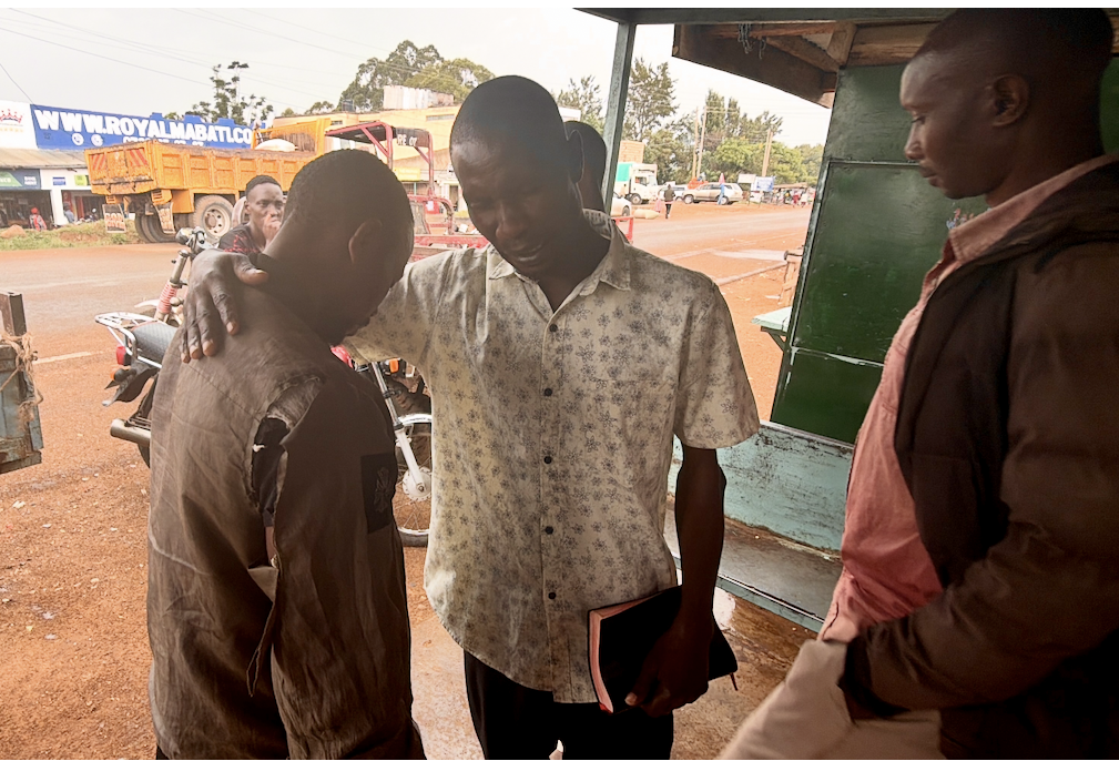 Believer praying over a man at a roadside shop