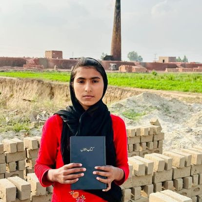 A young woman holding a Bible in front of a brick kiln in Pakistan
