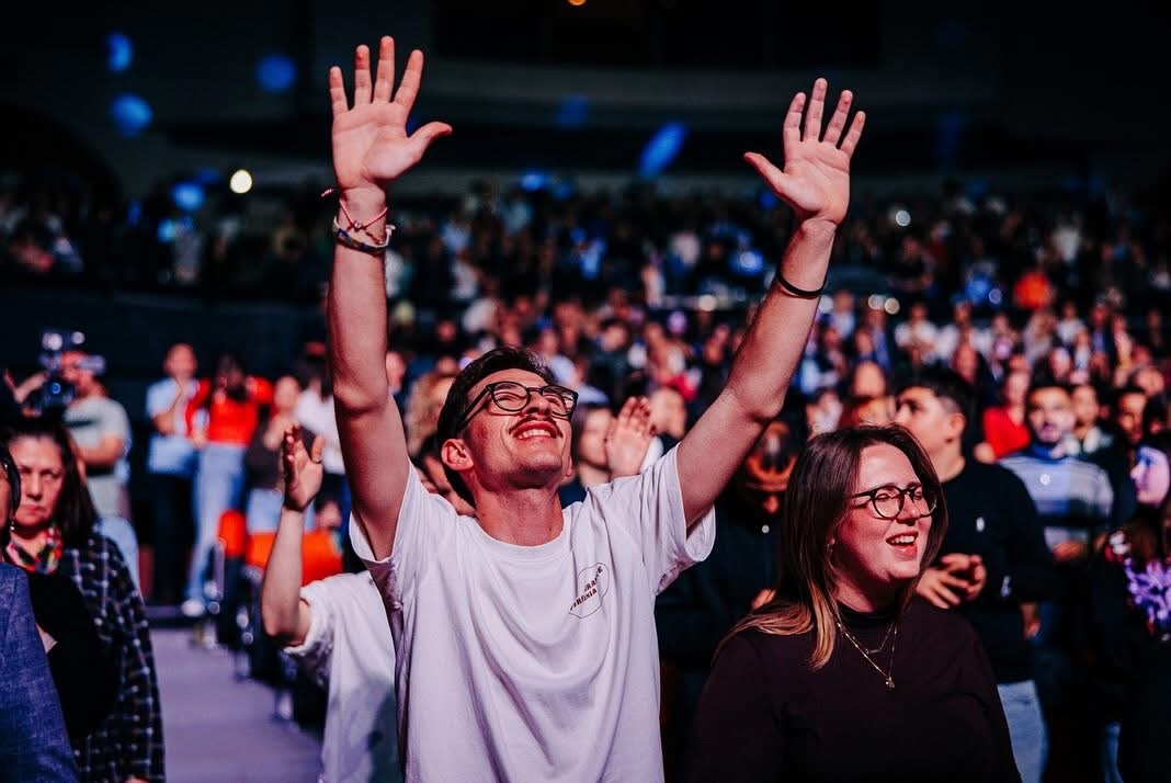 Young man worshiping with hands raised in a packed auditorium