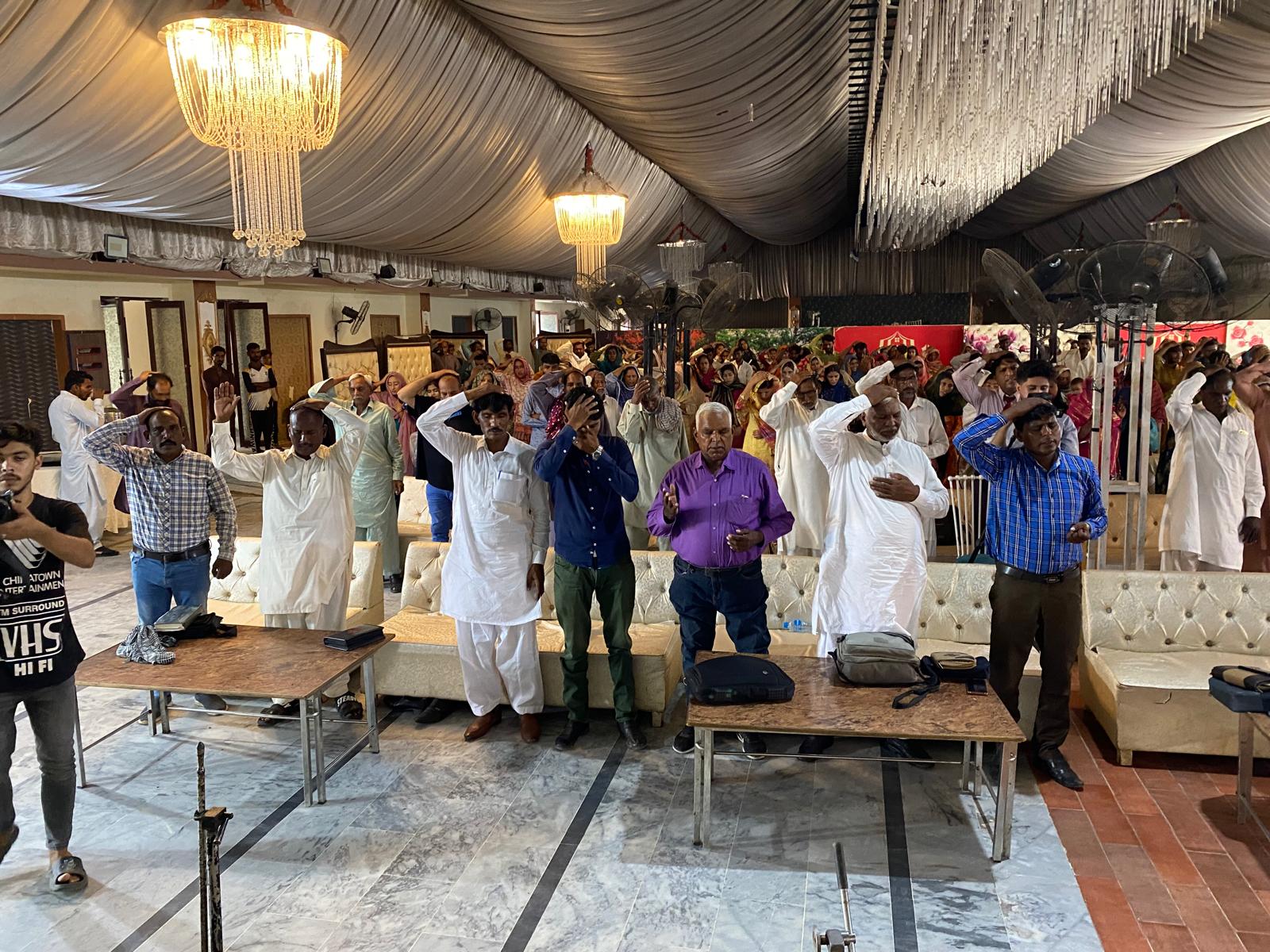 A congregation standing in prayer inside a decorated hall in Pakistan