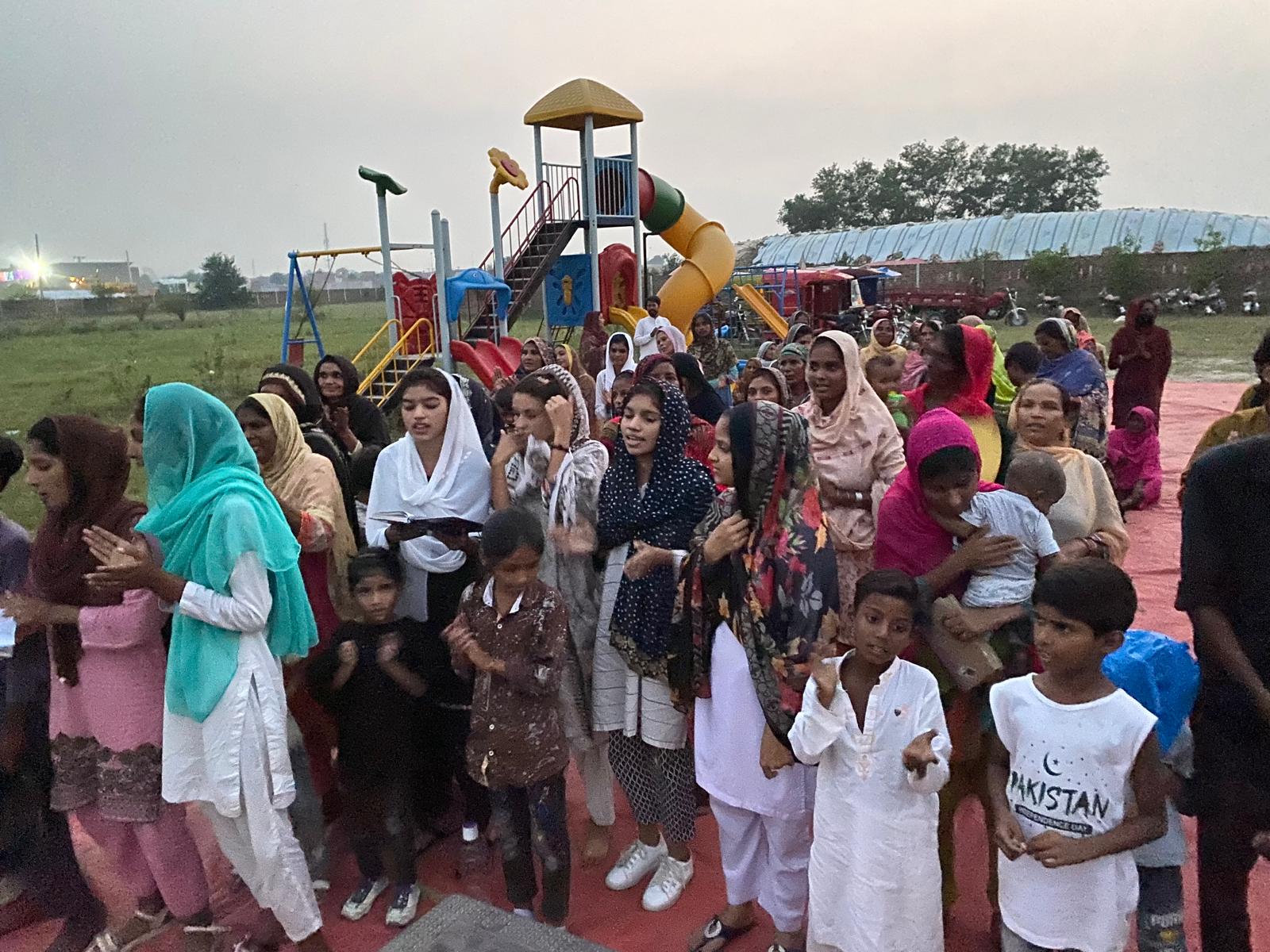 Women and children worshiping outdoors near a playground in Pakistan