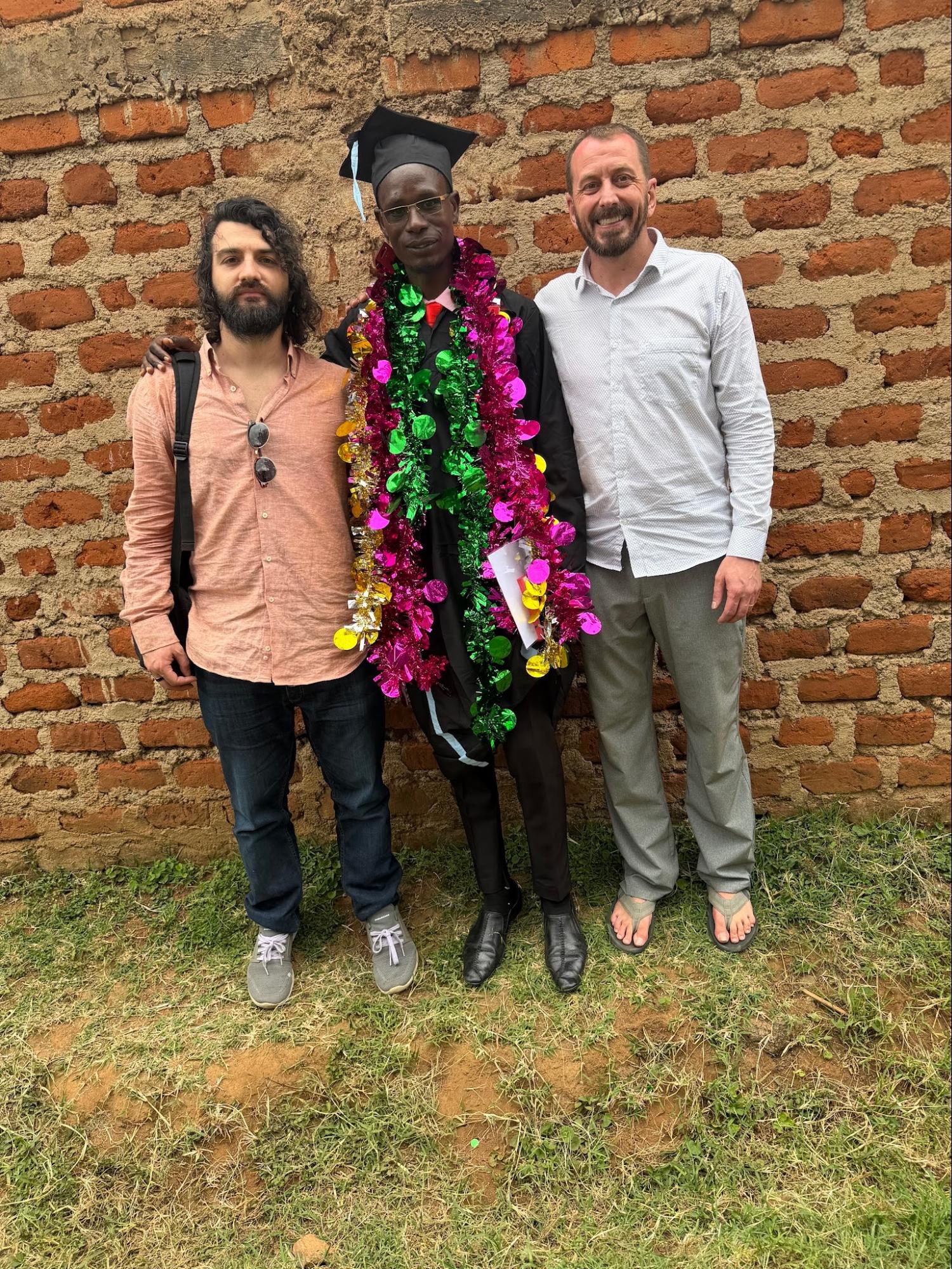 Graduate in cap and gown with team members outside a brick building